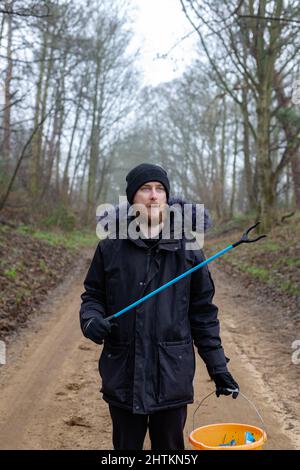 Un portrait d'un jeune barbu avec un picker de litière et un seau prêt à faire un ramassage de litière et nettoyer la campagne. Litières, déchets, envi Banque D'Images