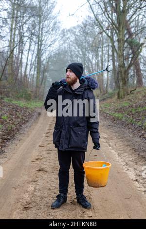 Un portrait d'un jeune barbu avec un picker de litière et un seau prêt à faire un ramassage de litière et nettoyer la campagne. Litières, déchets, envi Banque D'Images