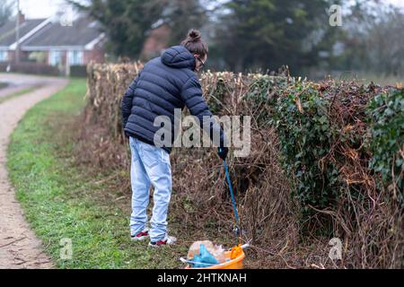 Un jeune homme équipé d'un préparateur de litière et d'un seau pour recueillir la litière et les ordures d'une voie de campagne. Collecte de litière, déchets, concept environnemental Banque D'Images