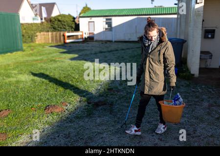 Un jeune homme avec un préparateur de litière et un seau pour recueillir la litière et les ordures d'un terrain de jeu de village. Collecte de litière, déchets, concept environnemental Banque D'Images