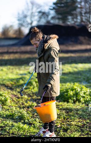Un jeune homme avec un préparateur de litière et un seau pour recueillir la litière et les ordures de la campagne. Collecte de litière, déchets, concept environnemental Banque D'Images