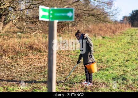 Un jeune homme avec un préparateur de litière et un seau pour recueillir la litière et les ordures de la campagne. Collecte de litière, déchets, concept environnemental Banque D'Images