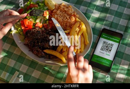 Femme au restaurant avec certificat de vaccination sur smartphone. L'état est valide. Banque D'Images