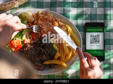 Femme au restaurant avec certificat de vaccination sur smartphone. L'état est valide. Banque D'Images