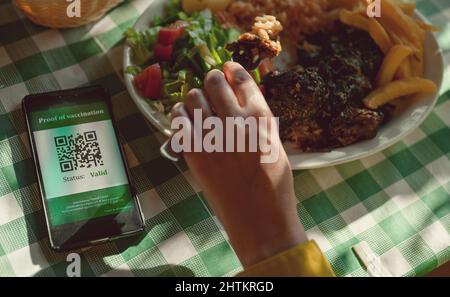 Femme au restaurant avec certificat de vaccination sur smartphone. L'état est valide. Banque D'Images