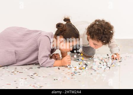 Bonne fille et garçon s'amusant ensemble pendant la fête d'anniversaire avec confetti. Les enfants adorables profitent de vacances et jettent des confettis. Banque D'Images