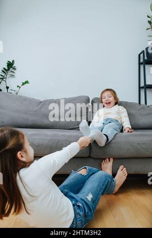 Forte fille faisant un effort physique, tirant hors de la chaussette d'un garçon, ils se préparent à une compétition de chatouillement. Il est assis sur un canapé dans un r vivant Banque D'Images