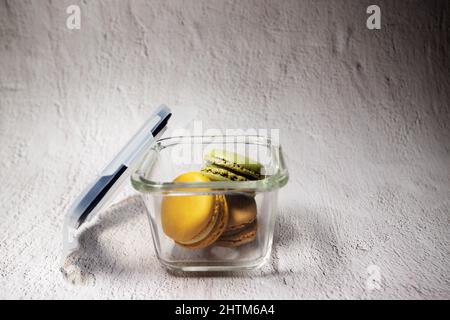 Colorer les macarons dans un récipient en verre avec couvercle ouvert sur un fond rustique clair Banque D'Images