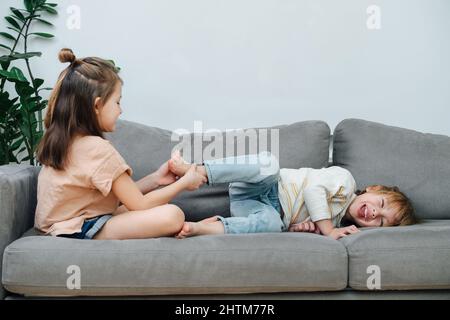 Une petite fille dominante chatouillant le pied du garçon, le faisant rouler et rire. Sur la vue latérale de la table. Banque D'Images
