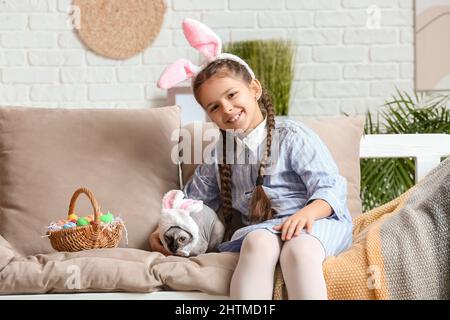 Petite fille avec chat Sphynx et oeufs de Pâques assis sur un canapé à la maison Banque D'Images