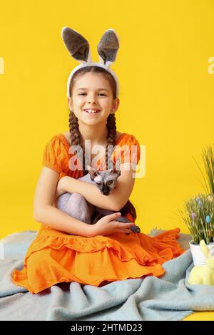 Petite fille dans les oreilles de lapin avec Sphynx chat sur fond jaune Banque D'Images