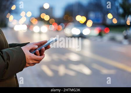 Image rapprochée des mains d'une femme utilisant un smartphone la nuit dans la rue de la ville, recherche ou concept de réseautage social, femme demandant le transport par Mo Banque D'Images