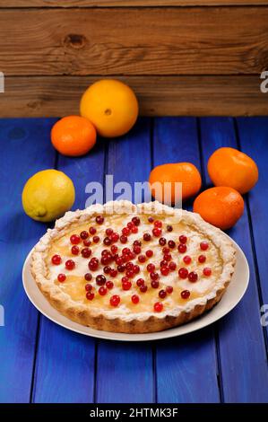 Tarte au citron ronde maison décorée de canneberges fraîches et d'orange, de citron et de clémentines entières sur une table verticale bleu profond Banque D'Images