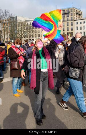 Femme en masque avec drapeau arc-en-ciel, symbole de paix. Les personnes avec des drapeaux et des pancartes ukrainiens protestent contre la guerre en Ukraine Banque D'Images