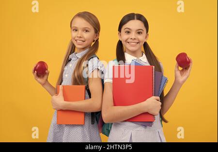 Les élèves heureux avec des livres contiennent des pommes bio vitamine fond jaune, petit déjeuner à l'école Banque D'Images