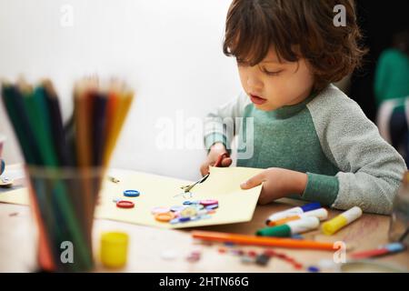 Faire preuve de créativité avec la découpe. Un petit garçon mignon faisant de l'artisanat à la pré-école. Banque D'Images