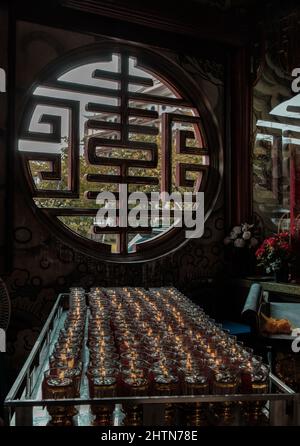 La lumière brille à travers une fenêtre circulaire de style chinois avec de nombreuses bougies votives rouges à l'intérieur du temple chinois. Mise au point et flou. Banque D'Images