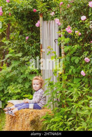 Enfant sur une botte de foin avec des biscuits et du lait. Petite fille drôle. Enfant insouciant. La petite fille aime la vie et la nature. Bonne enfance. Banque D'Images