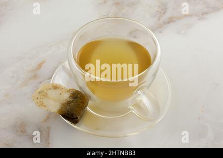 Thé au gingembre citron dans une tasse en verre isolée avec un teabag usagé sur la soucoupe Banque D'Images