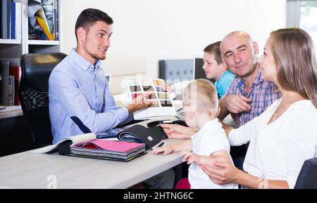 Vendeur positif dans le magasin de meubles aidant la jeune famille dans le choix Banque D'Images