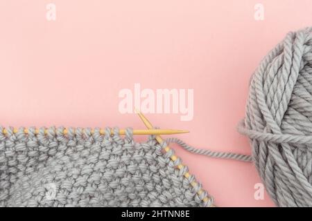 Morceau de tissu tricoté gris sur aiguilles en bois de bambou avec boule de fil, procédé de tricotage sur fond rose. Copier l'espace pour le texte .vue de dessus Flat lay Banque D'Images