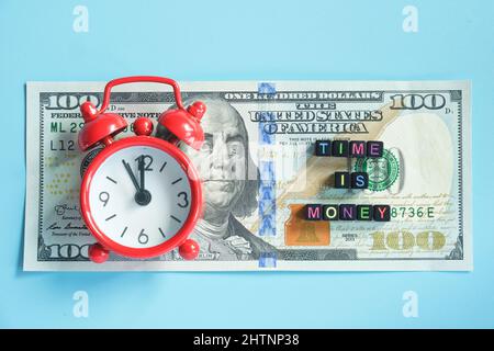 Le temps est le texte d'argent et le réveil rouge sur le fond des factures américaines de centaines de dollars, de gros plan. Citation créative du jour. Vue de dessus Flat lay Banque D'Images