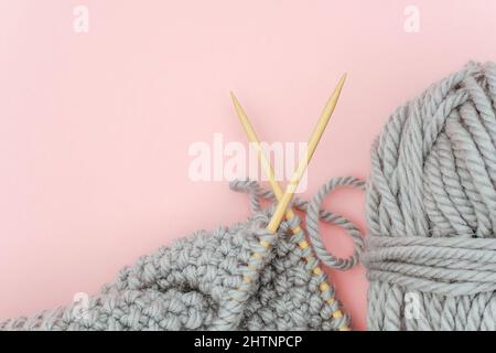 Morceau de tissu tricoté gris sur aiguilles en bois de bambou avec boule de fil, procédé de tricotage sur fond rose. Copier l'espace pour le texte .vue de dessus Flat lay Banque D'Images