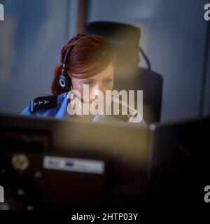 Une femme de police dans un centre d'appels, écoutant attentivement un appel d'urgence d'une personne en détresse Banque D'Images