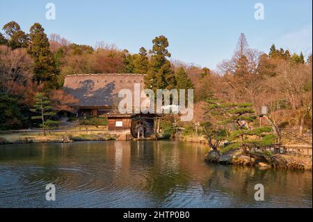 Vue sur la maison et le moulin à eau de style Gassho sur l'étang d'Okuike dans le zoo de Higashiyama et le jardin botanique dans la lumière du soir. Nagoya. Japon Banque D'Images