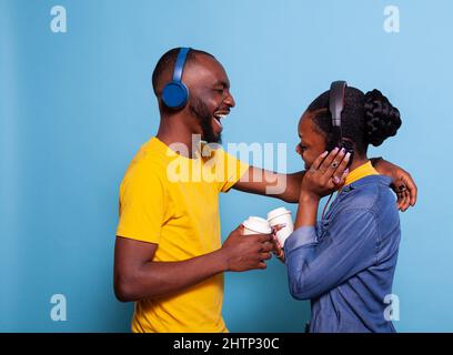 Petite amie et petit ami chantant et s'amuser avec la chanson sur le casque, en appréciant la musique de liste de lecture. Couple joyeux écoutant le son mp3 sur le micro-casque, souriant et l'un l'autre en studio. Banque D'Images