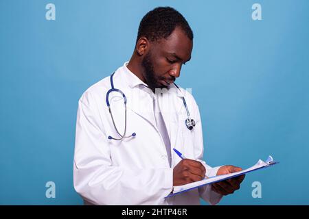 Portrait d'un médecin professionnel avec stéthoscope tenant un écritoire sur le dossier du patient en consultation clinique. Medic en blouse de laboratoire blanche, en regardant l'histoire médicale et en prenant des notes. Banque D'Images