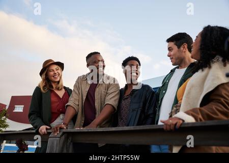 Un groupe d'amis tendance et varié se tenant et discutant ensemble sur le toit lors d'une fête en ville Banque D'Images