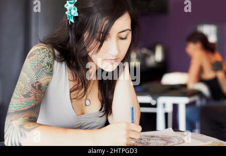 Des modèles exceptionnels. Une artiste de tatouage féminine dessinant un nouveau design dans son salon de tatouage. Banque D'Images