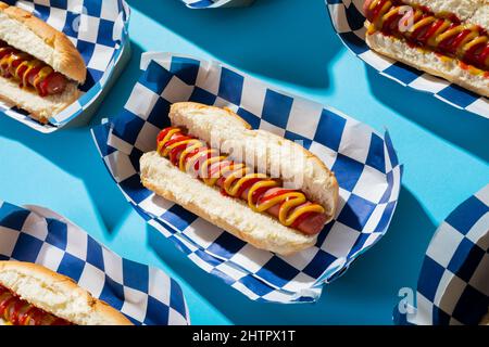 Gros plan grand angle des hot dogs dans des récipients disposés sur fond bleu Banque D'Images