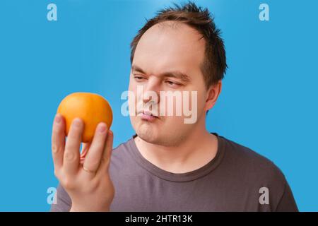 Portrait d'un homme adulte avec un fruit orange dans sa main, fond de studio bleu Banque D'Images