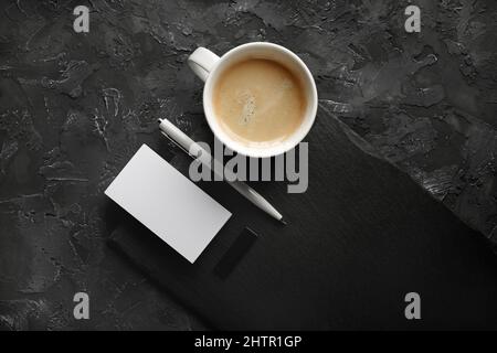 Photo d'une carte de visite vierge, d'une tasse à café, d'un stylo, d'une clé usb et d'une plaque en ardoise sur fond de pierre noire. Banque D'Images