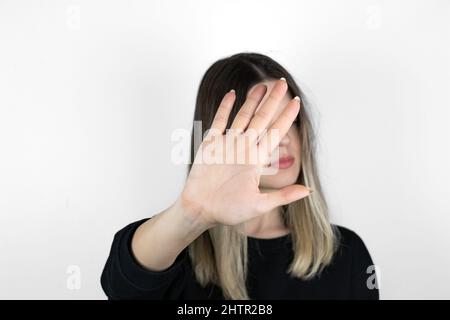 Une fille blonde portant des vêtements décontractés fait un signe d'arrêt. Arrière-plan blanc. Son visage n'est pas visible. Personne méconnaissable. Pas de photo de concept de violence. Banque D'Images