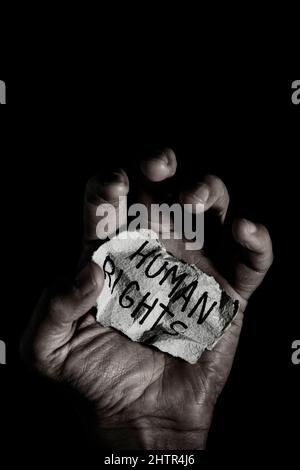 gros plan d'un homme avec un morceau de papier dans sa main qui lit le texte des droits de l'homme, sur fond noir, avec une lumière dramatique Banque D'Images