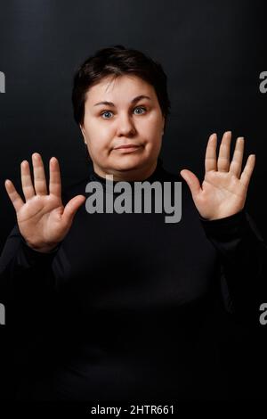 brunette femme étire ses paumes vers l'avant sur un fond noir. stop geste. Photo de haute qualité Banque D'Images