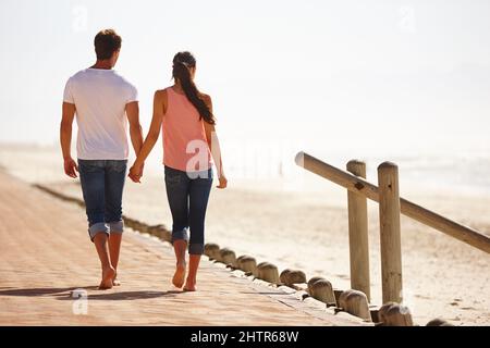 En vous promenant sur la voie de la mémoire. Vue arrière photo d'un jeune couple marchant le long de la plage en tenant les mains. Banque D'Images