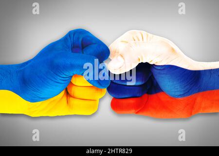 Concept du conflit entre la Russie et l'Ukraine avec des poings peints dans les couleurs du drapeau se confrontant sur fond gris isolé Banque D'Images