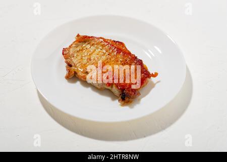 Un morceau de viande frite sur une assiette blanche. Mauvais aliment gras. Arrière-plan blanc. Un morceau de boule de porc frite dans le beurre. Minimalisme Banque D'Images