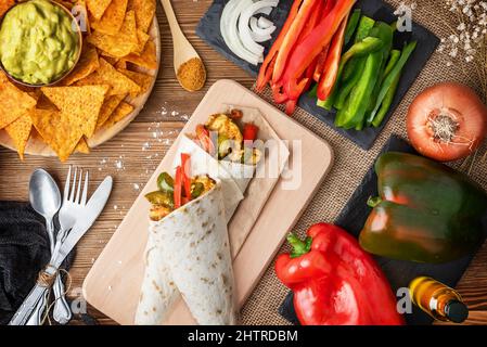 Fajitas au poulet avec poivrons, oignons et épices et sauce guacamole avec chips de tortilla ou nachos sur une table en bois Banque D'Images