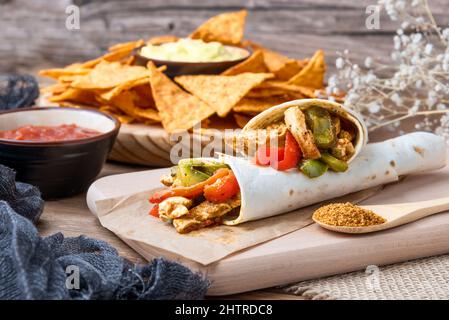 Gros plan de fajitas au poulet avec poivrons, oignons et épices et sauce guacamole avec chips de tortilla ou nachos sur une table en bois Banque D'Images