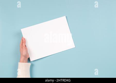 Les femmes tiennent une feuille de papier blanc vierge sur fond bleu clair.Vue de dessus.Maquette de papier avec espace de copie pour le texte Banque D'Images