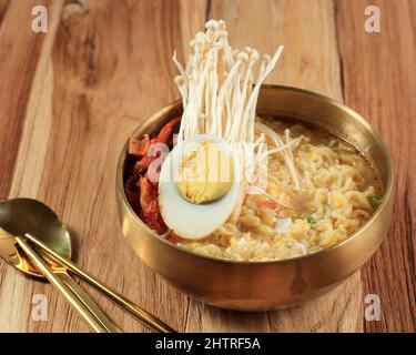 Style coréen Instant Noodle, Ramyeon ou Ramyun avec saveur épicée recouvert d'œuf à moitié cuit, de museau et de Kimchi. Sur une table en bois Banque D'Images