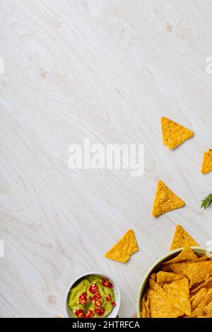 Sauce à trempette verte avec piments rouges de nacho chips dans un bol sur la table avec espace vide Banque D'Images