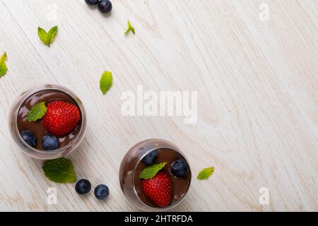 Fraises, bleuets et feuilles de menthe avec dessert au chocolat dans des bols sur la table avec espace vide Banque D'Images