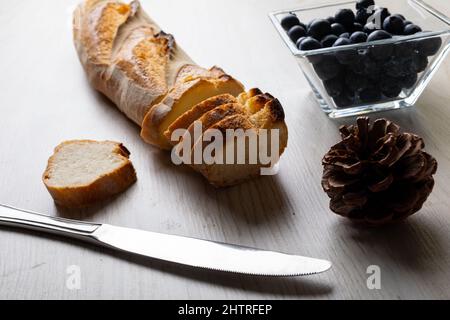 Gros plan de baguette en tranches avec cône de pin et couteau de table avec myrtilles dans un bol sur la table Banque D'Images