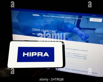 Personne tenant un smartphone avec le logo de la société espagnole Laboratorios Hipra S.A. à l'écran devant le site. Mise au point sur l'affichage du téléphone. Banque D'Images